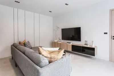 Modern living room with sleek design and wall-mounted TV, featuring a stylish gray sofa and minimalist decor.