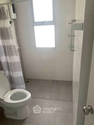 Modern bathroom with shower and window, featuring neutral tiles and striped curtain.