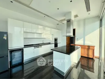 Modern kitchen with sleek white cabinetry and black countertops, featuring an island and built-in appliances.