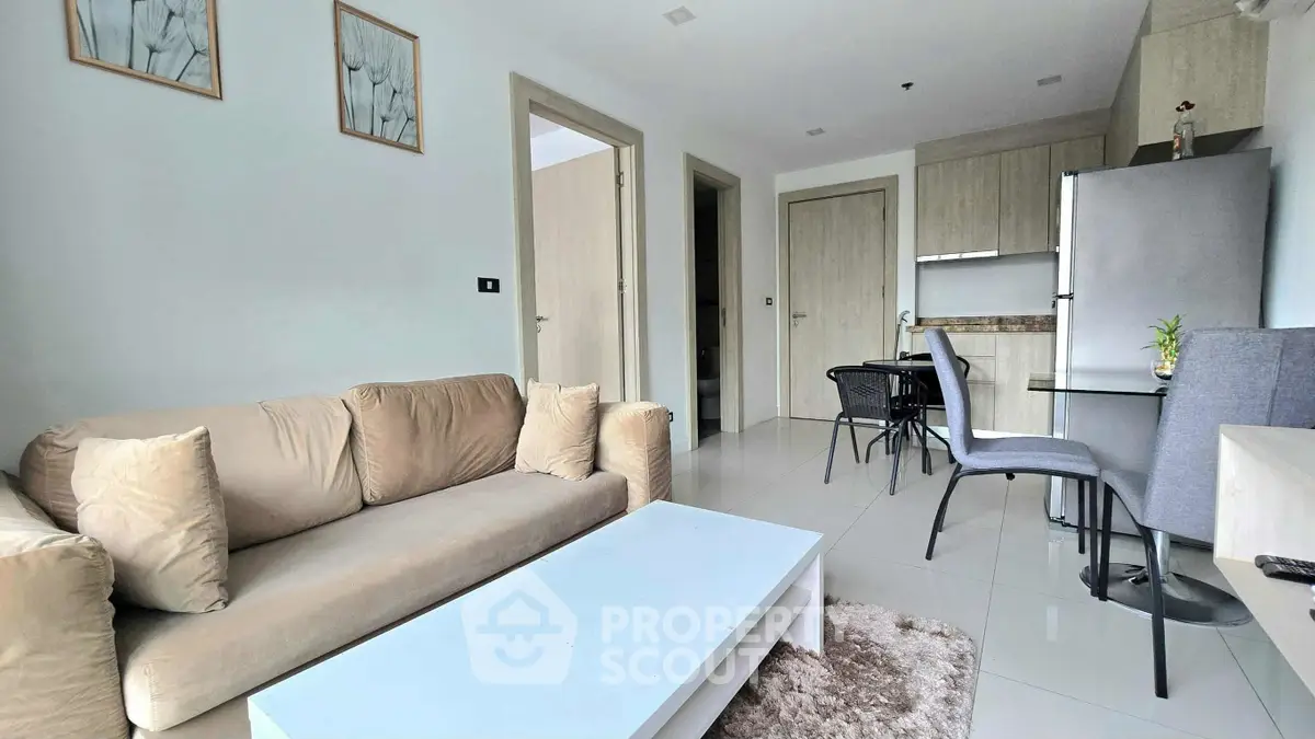 Modern living room with beige sofa, sleek kitchen, and dining area in open layout apartment.