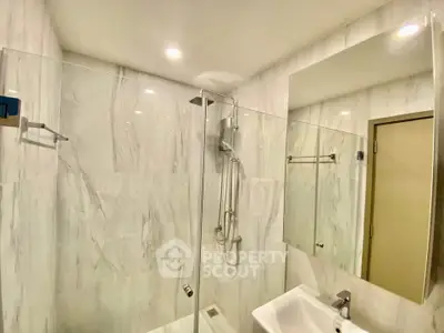 Modern bathroom with glass shower and marble walls, featuring sleek fixtures and bright lighting.