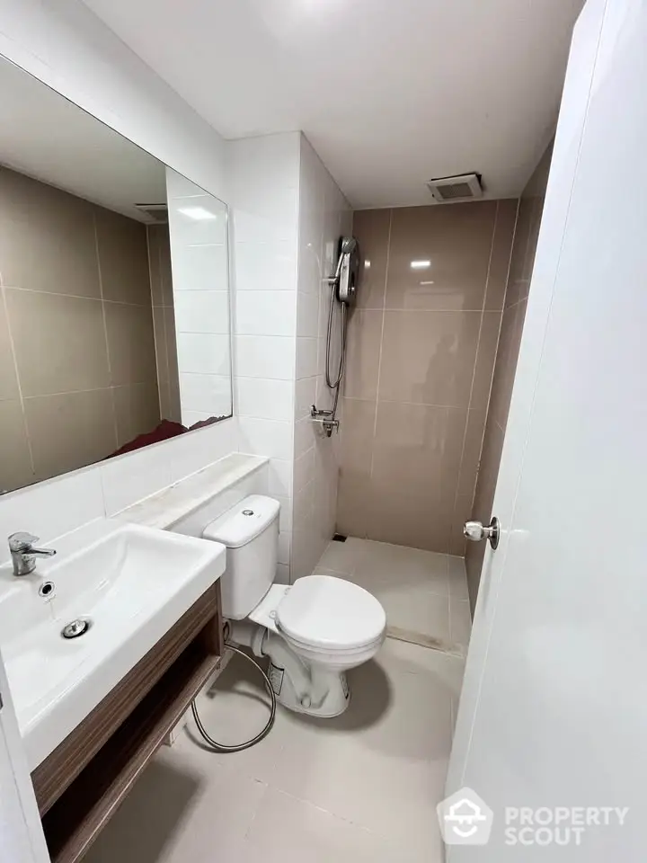 Modern bathroom with sleek design featuring a shower, sink, and toilet in neutral tones.