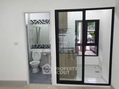 Modern apartment with compact bathroom and glass-enclosed kitchen area, ideal for urban living.