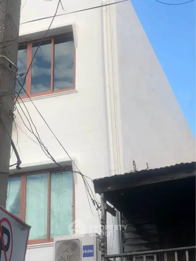 Modern white building exterior with large windows and air conditioning unit, showcasing minimalist architecture.