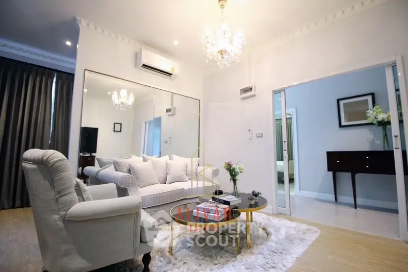 Elegant living room with plush white sofas, chic chandelier, and mirrored wall creating a spacious, luxurious ambiance perfect for upscale living.
