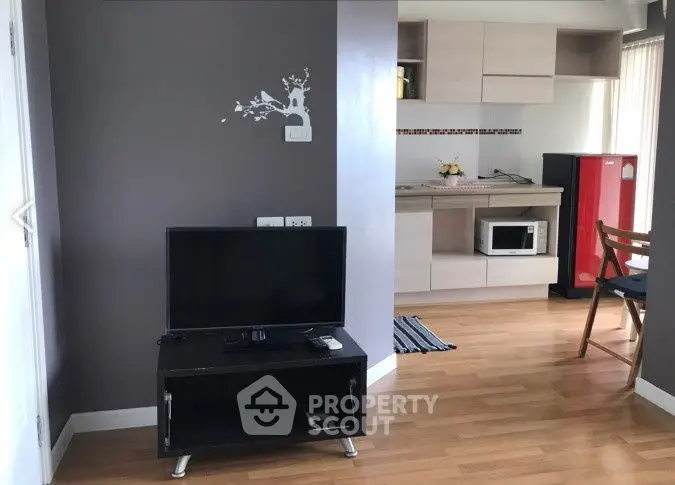 Modern living room with TV and open kitchen layout, featuring wooden flooring and stylish decor.