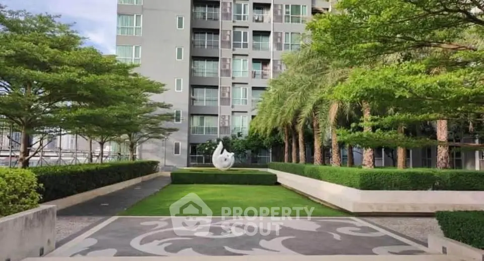 Modern apartment building with lush landscaped garden and artistic sculpture.