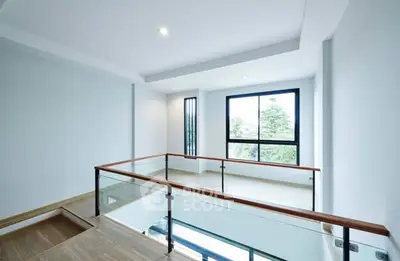 Modern open-plan interior with large windows and glass railing, offering a bright and airy atmosphere.