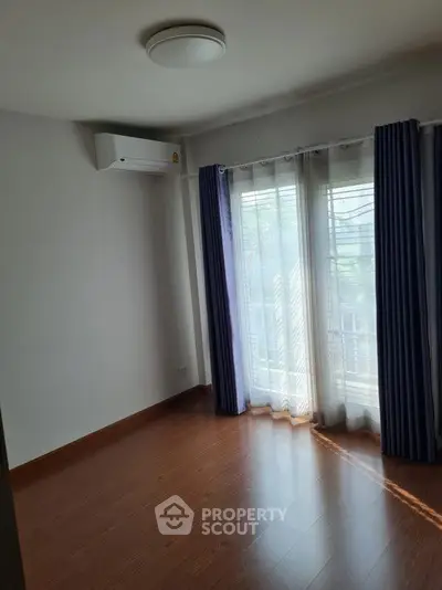 Bright empty room with hardwood floors and large window with curtains.