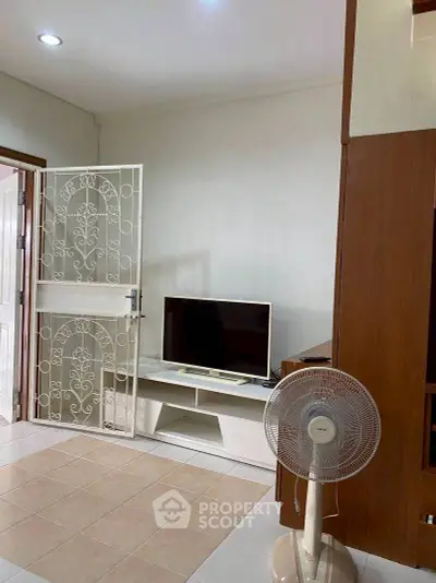 Cozy living room with TV and fan, featuring elegant tiled flooring and decorative door.