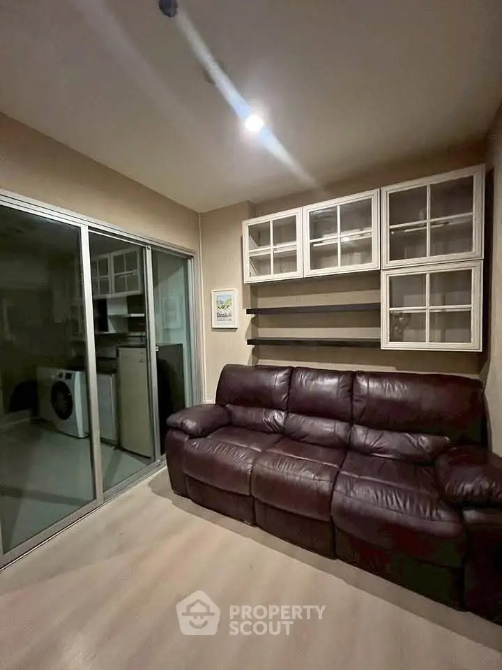 Cozy living room with leather sofa and glass cabinets, adjacent to a modern kitchen with appliances.