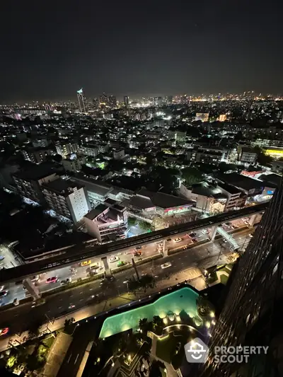 Stunning night cityscape view from high-rise building with illuminated pool and bustling streets below.