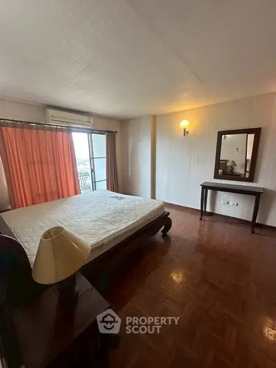 Spacious bedroom with parquet flooring and large window for natural light.