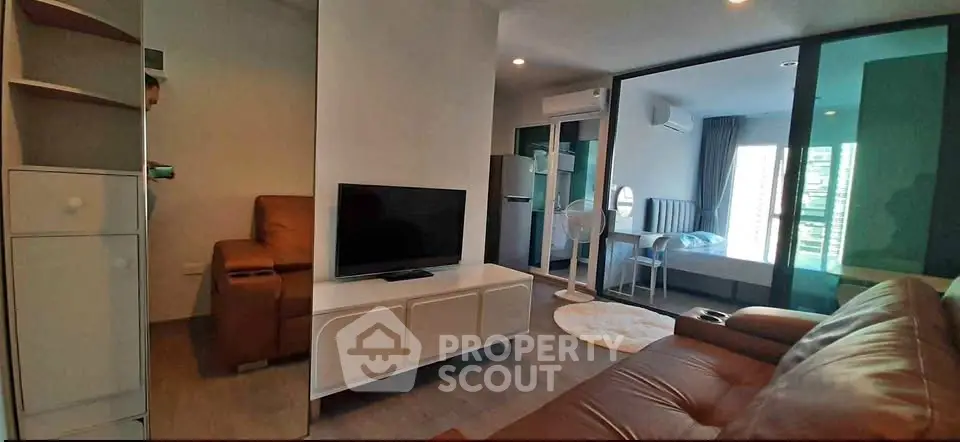 Modern living room with leather sofas and TV, open to a bedroom with glass sliding doors.