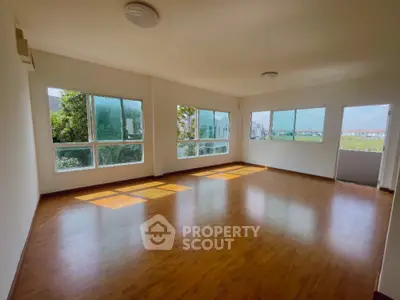 Spacious sunlit room with large windows and hardwood floors, perfect for versatile living space.