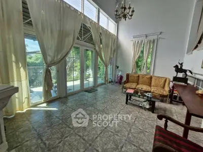 Spacious living room with high ceilings and large windows opening to a lush garden view.