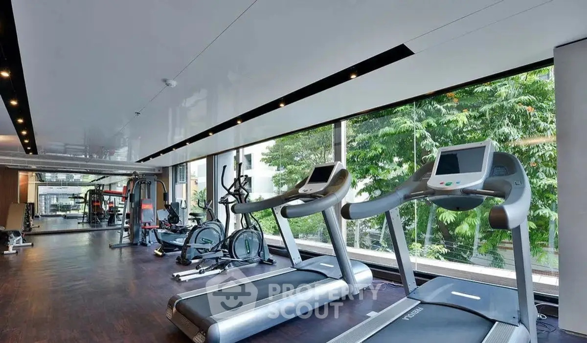 Modern gym with treadmills and exercise equipment in a bright, spacious room with large windows.