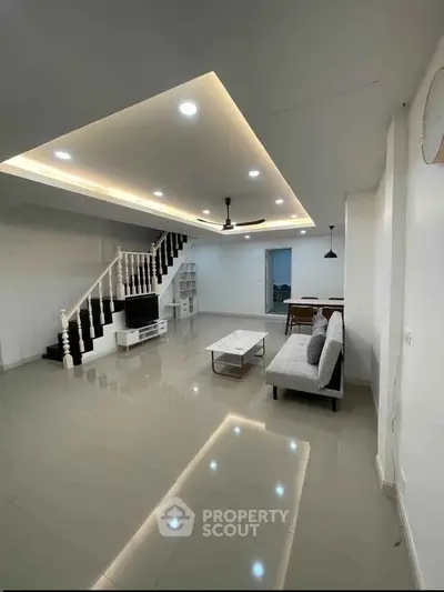 Spacious modern living room with sleek design and elegant staircase, perfect for family gatherings.