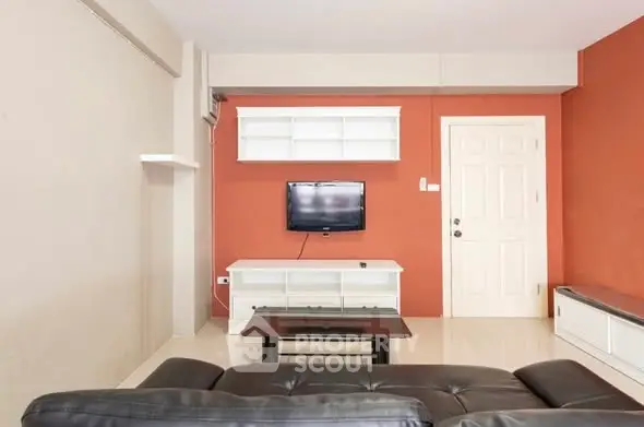 Modern living room with sleek black leather sofa and wall-mounted TV, featuring a vibrant orange accent wall.