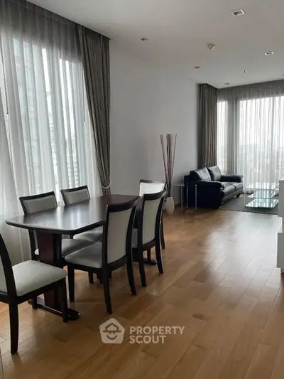 Spacious modern living room with dining area, wooden flooring, and large windows offering natural light.