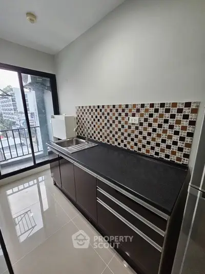 Modern kitchen with sleek cabinetry and mosaic backsplash in a bright apartment with balcony view.