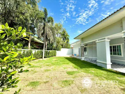 Spacious backyard with lush greenery and modern house exterior under clear blue sky.