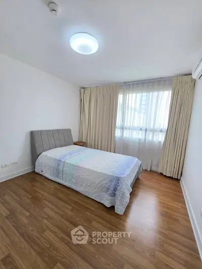 Spacious bedroom with wooden flooring and large window in modern apartment