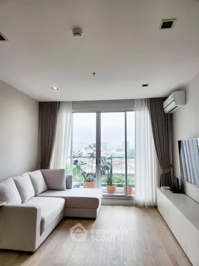 Modern living room with large window and city view, featuring a cozy white sofa and sleek TV setup.