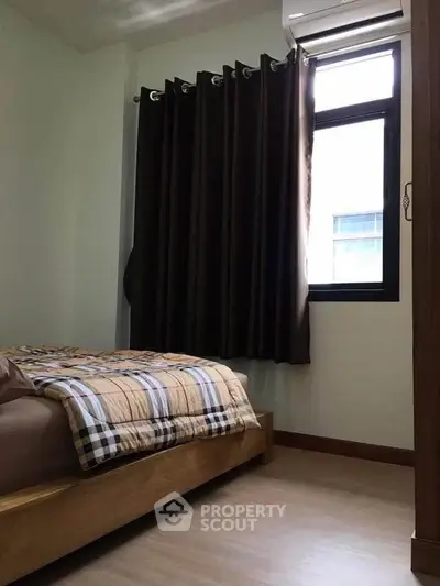 Cozy bedroom with wooden bed frame and large window with dark curtains.