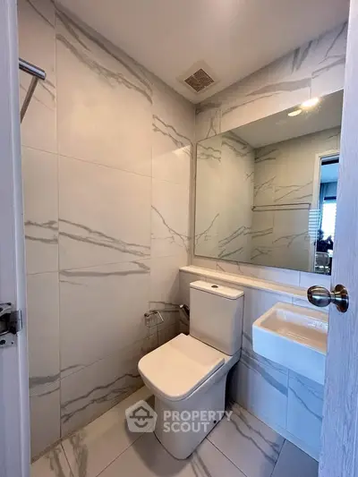 Modern bathroom with sleek design and marble tiles, featuring a compact toilet and stylish sink.