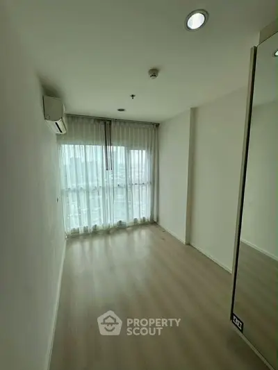 Spacious empty room with large window and wooden flooring, perfect for customization.