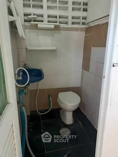 Compact bathroom with blue sink and white toilet in a tiled space.