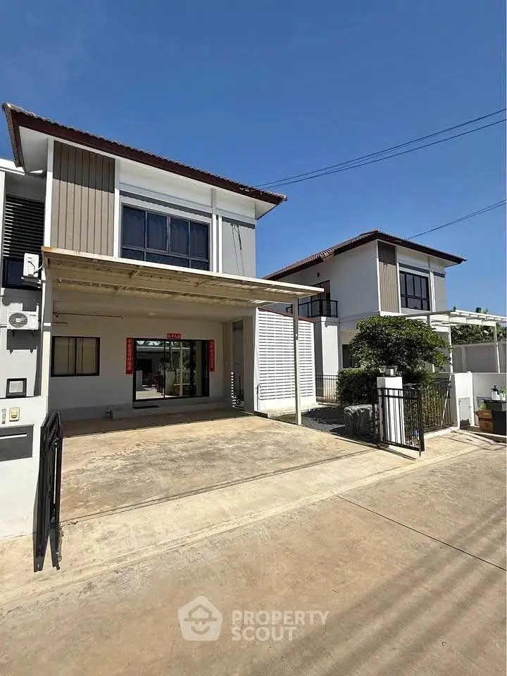 Modern two-story house with driveway and gated entrance under clear blue sky.