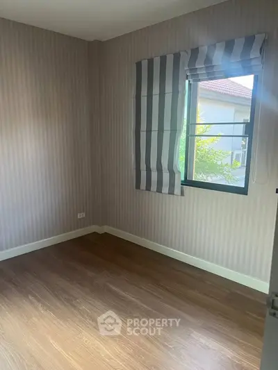 Cozy empty bedroom with wooden flooring and striped curtains, perfect for customization.