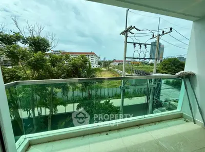 Spacious balcony with glass railing offering a serene view of lush greenery and urban landscape.