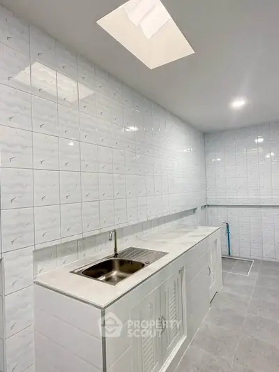 Modern kitchen with sleek white tiles and skylight, featuring a stainless steel sink and ample counter space.