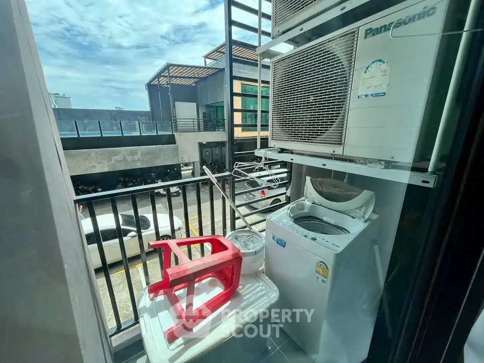 Compact balcony with washing machine and air conditioning unit, overlooking parking area.