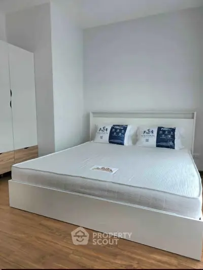 Modern bedroom with sleek white bed and wooden flooring, perfect for a cozy retreat.