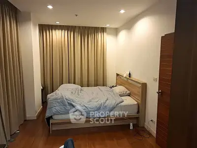 Cozy bedroom with wooden flooring and soft lighting, featuring a comfortable bed and elegant curtains.