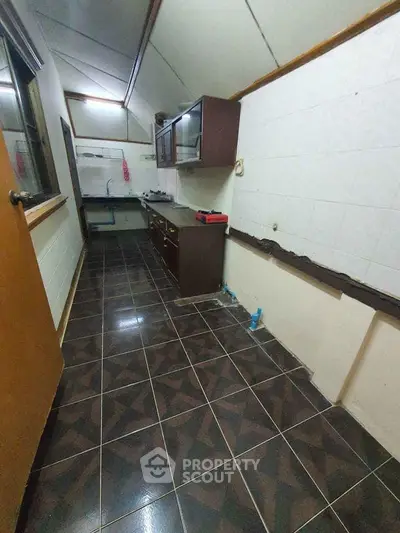 Narrow kitchen with dark tiled floor and wooden cabinets, ideal for compact spaces.