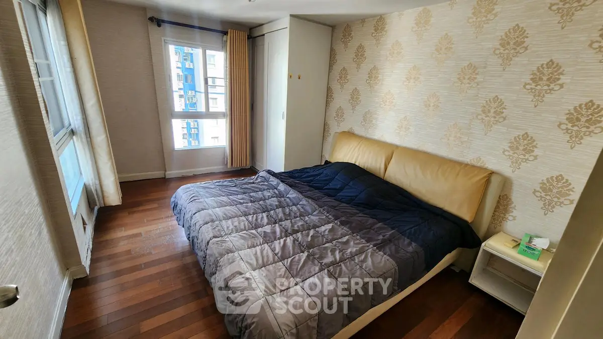 Cozy bedroom with elegant wallpaper and wooden flooring, featuring a comfortable bed and natural light.