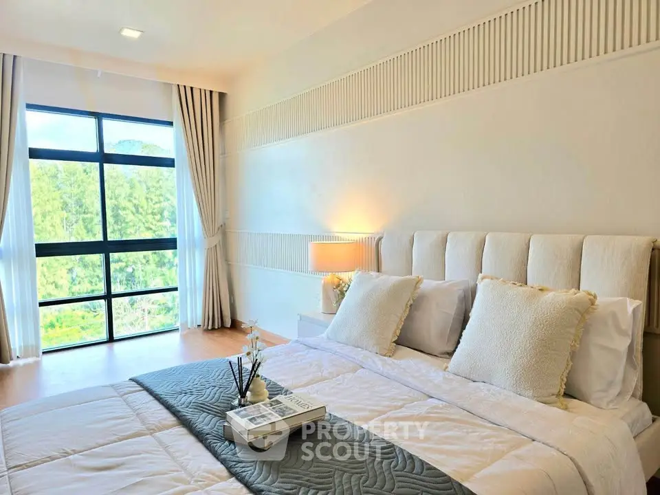 Spacious bedroom with large window offering stunning green views, elegant decor, and cozy ambiance.