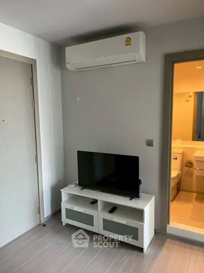 Modern living room with air conditioning and TV unit next to a bathroom entrance.