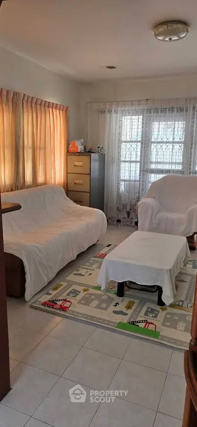 Cozy living room with natural light, tiled floor, and comfortable seating, perfect for relaxation.