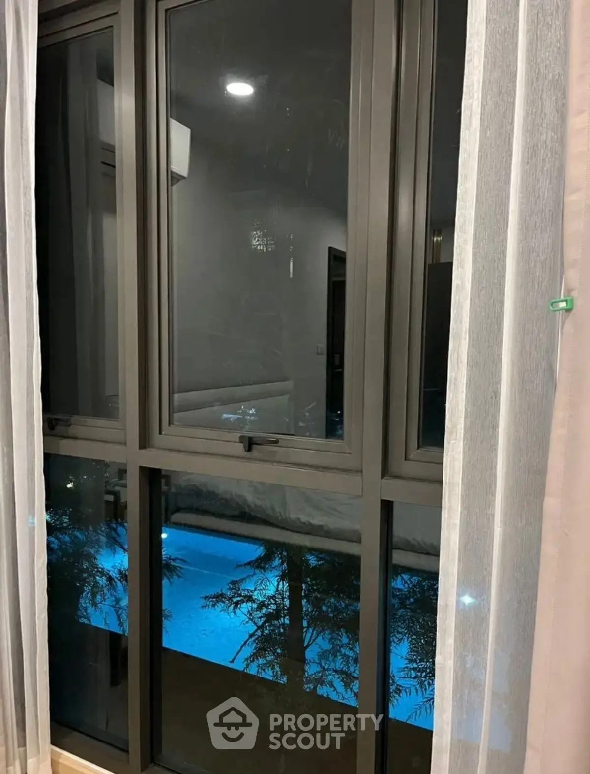 Modern window view overlooking illuminated pool at night, perfect for serene evenings.