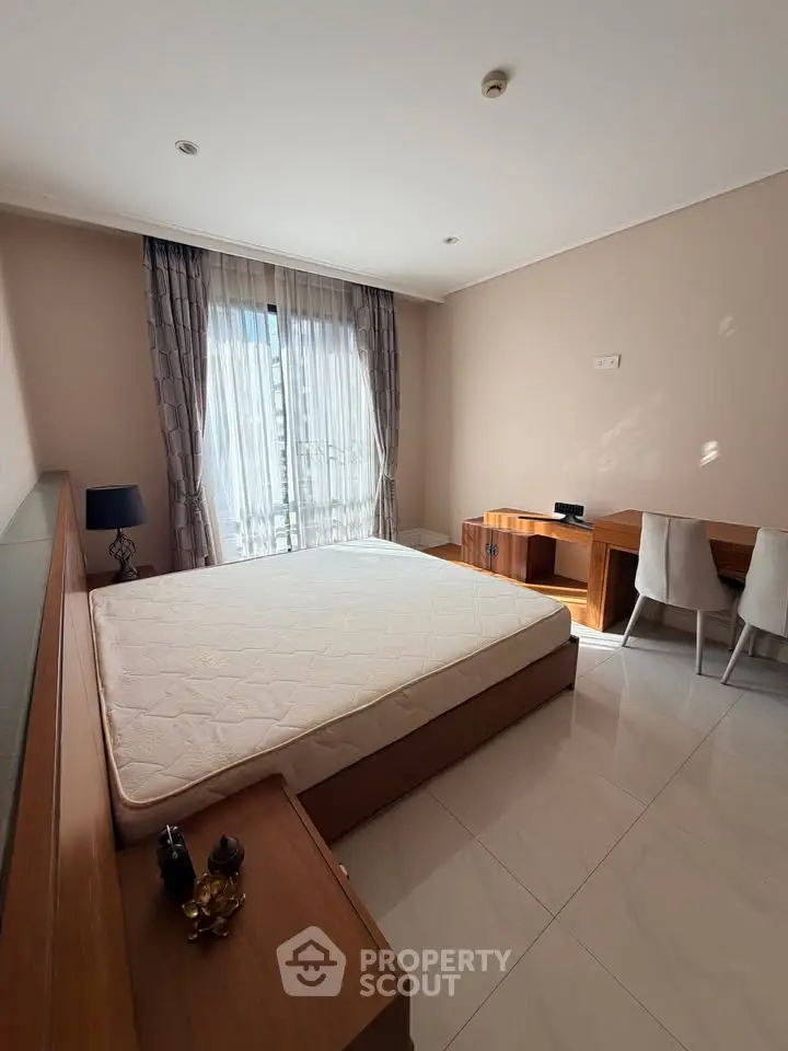Spacious bedroom with natural light, featuring a large bed and elegant wooden furniture.