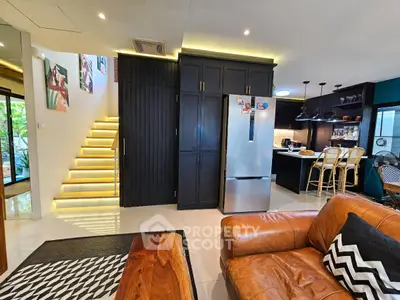 Stylish modern living room with open kitchen and staircase, featuring chic decor and cozy seating.