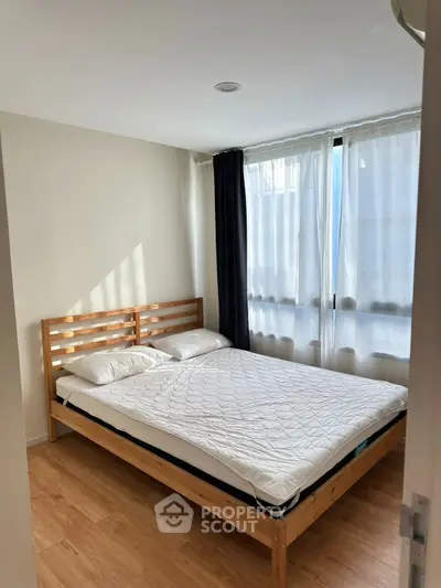 Cozy bedroom with wooden flooring and natural light through large windows.