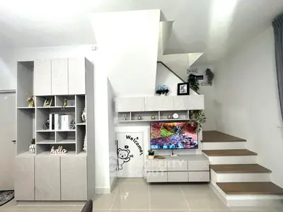 Modern living room with stylish staircase and built-in storage, featuring a vibrant wall-mounted TV display.