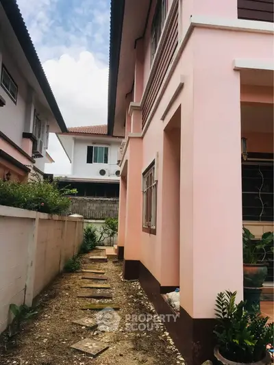 Charming pink exterior of a two-story house with a side pathway and lush greenery.